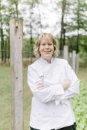 Sherry Ronning in a chef coat standing up against a garden fence.