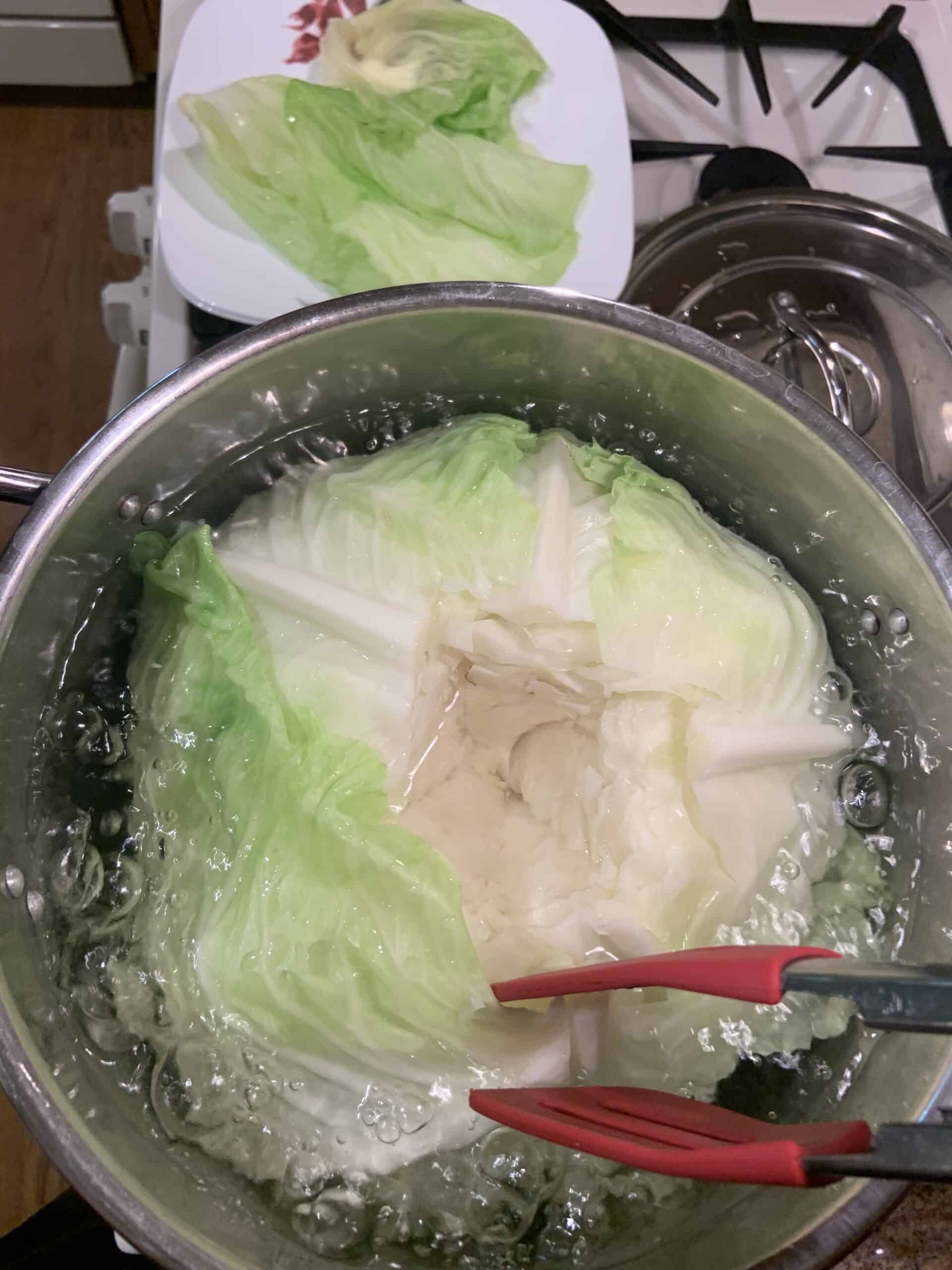 Peeling leaves off of the cabbage head while in the pot of boiling water.