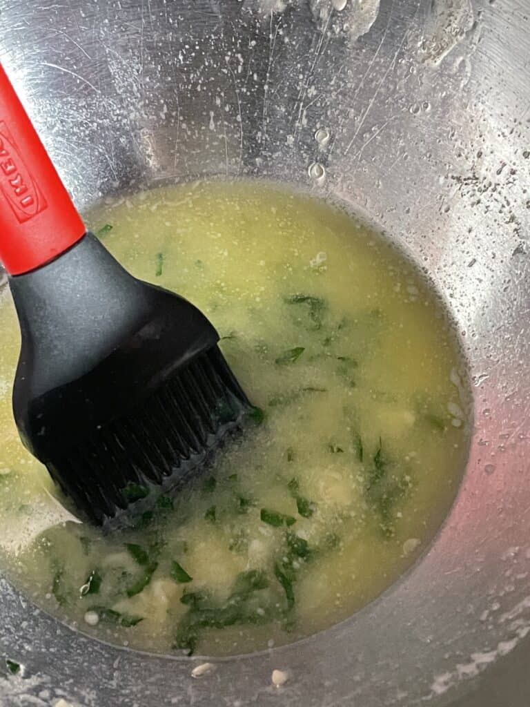 Melted Garlic Parsley Butter in a bowl with a pastry brush.