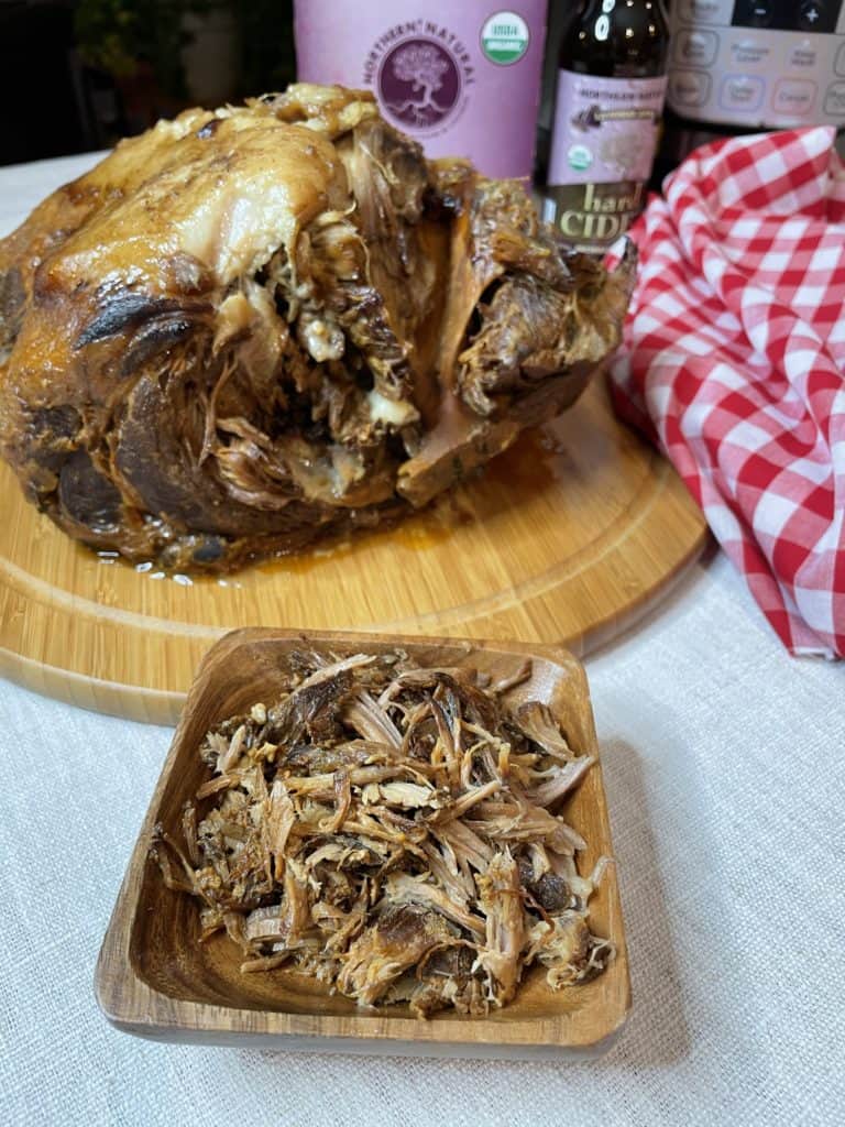 Instant Pot Pulled Pork on a wooden board along with a bowl of shredded pork.
