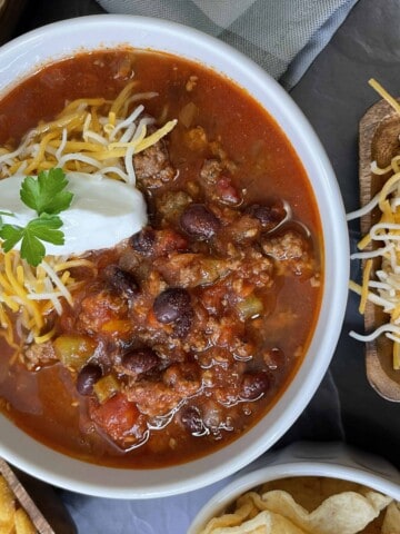 Best Venison Chili Recipe in a white bowl surrounded by different toppings.