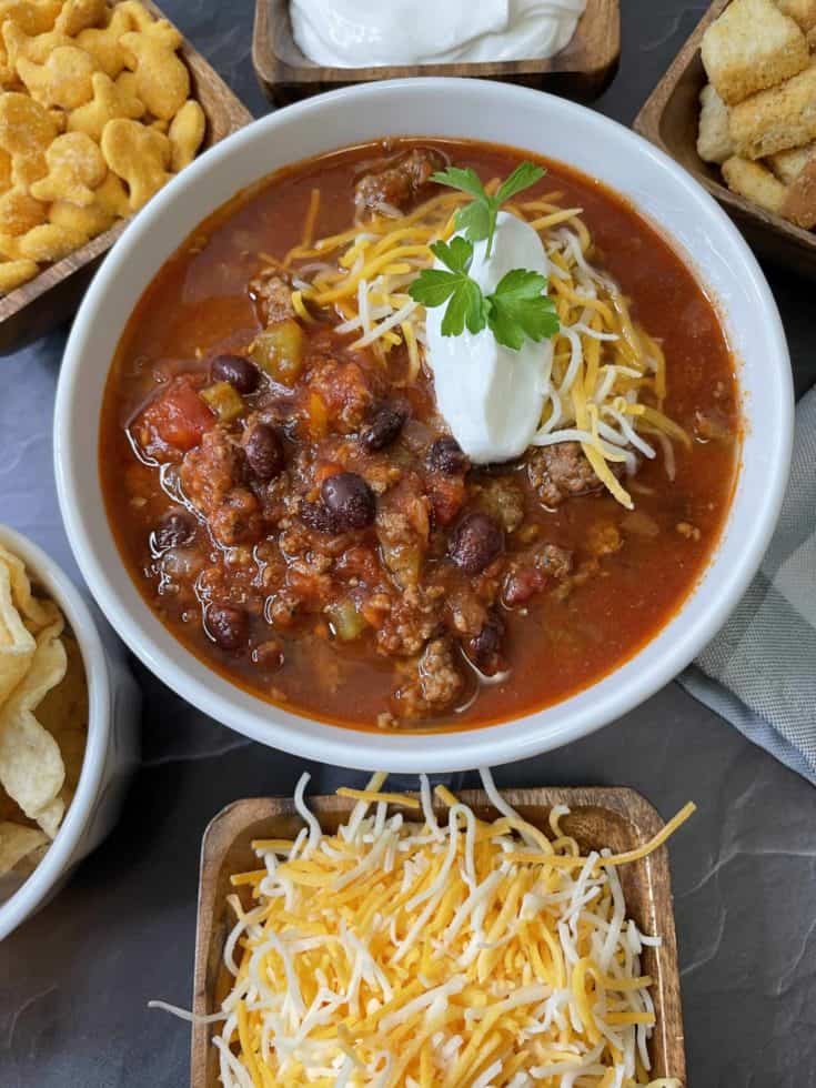 Best Venison Chili Recipe in a white bowl surrounded by different toppings.