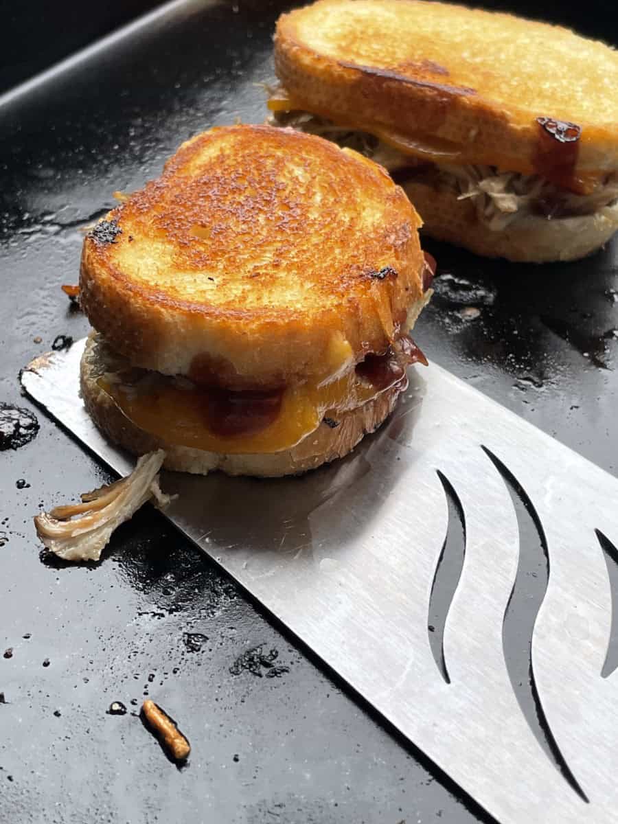 Pulled Pork Blackstone Grilled Cheese cooking on the griddle being removed with a griddle spatula.