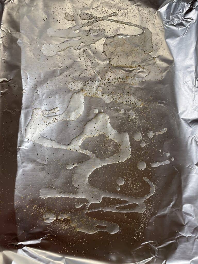 Seasoned olive oil drizzled on a foil lined baking sheet.