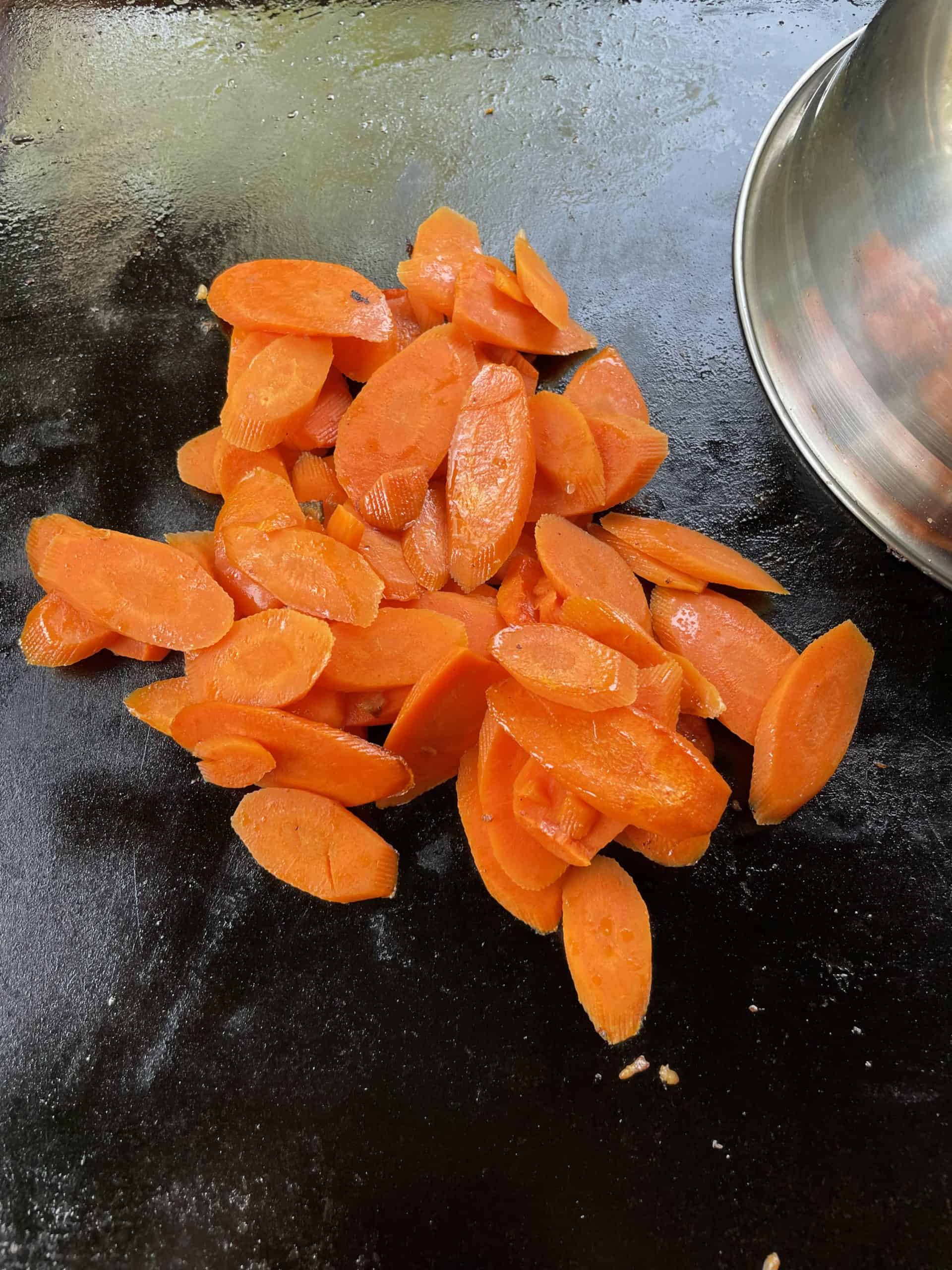 On a hot griddle, place the carrots and add some water.  Cover with a dome lid to steam and cook the carrots.