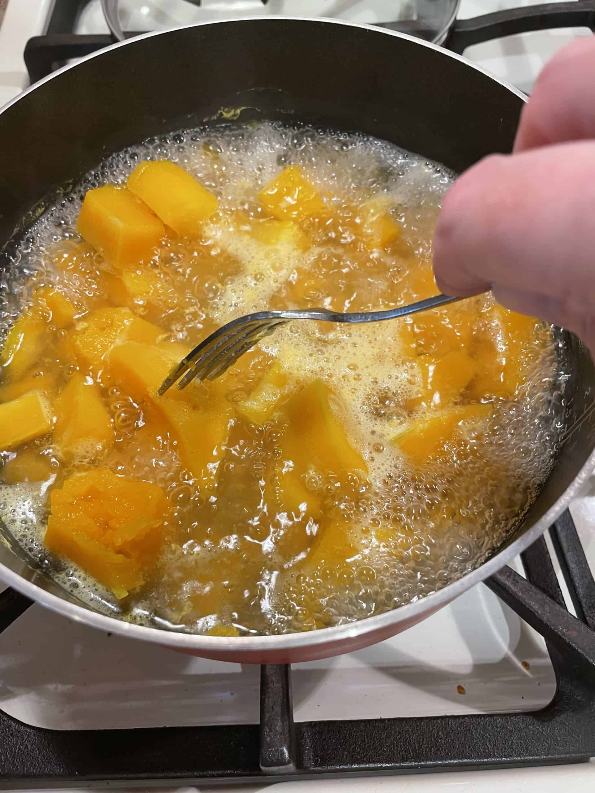 Testing mashed butternut squash with a fork for doneness.