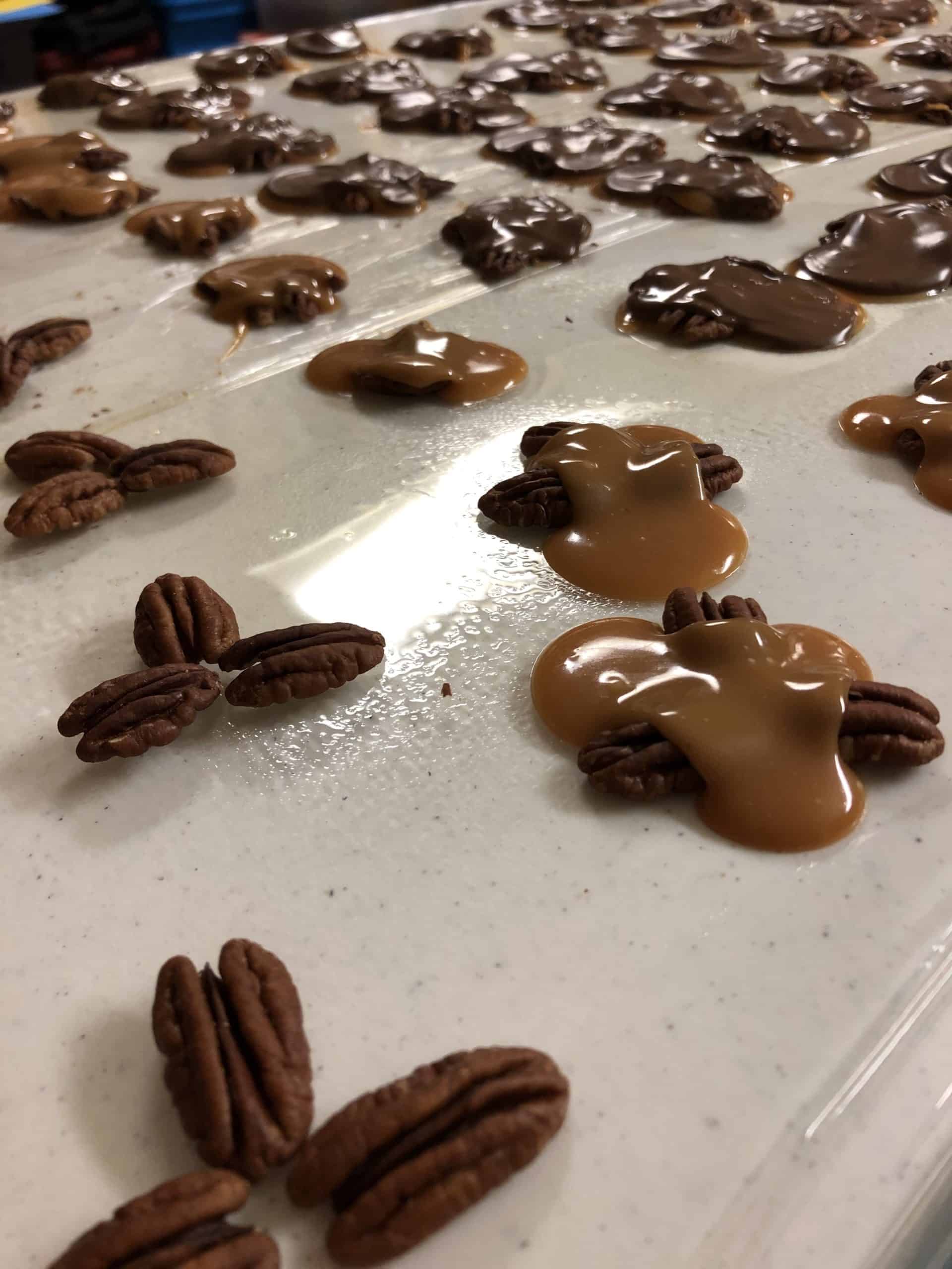 Pecans arranged in a cluster on a plastic wrapped, greased table and then topped with the homemade caramel and chocolate.