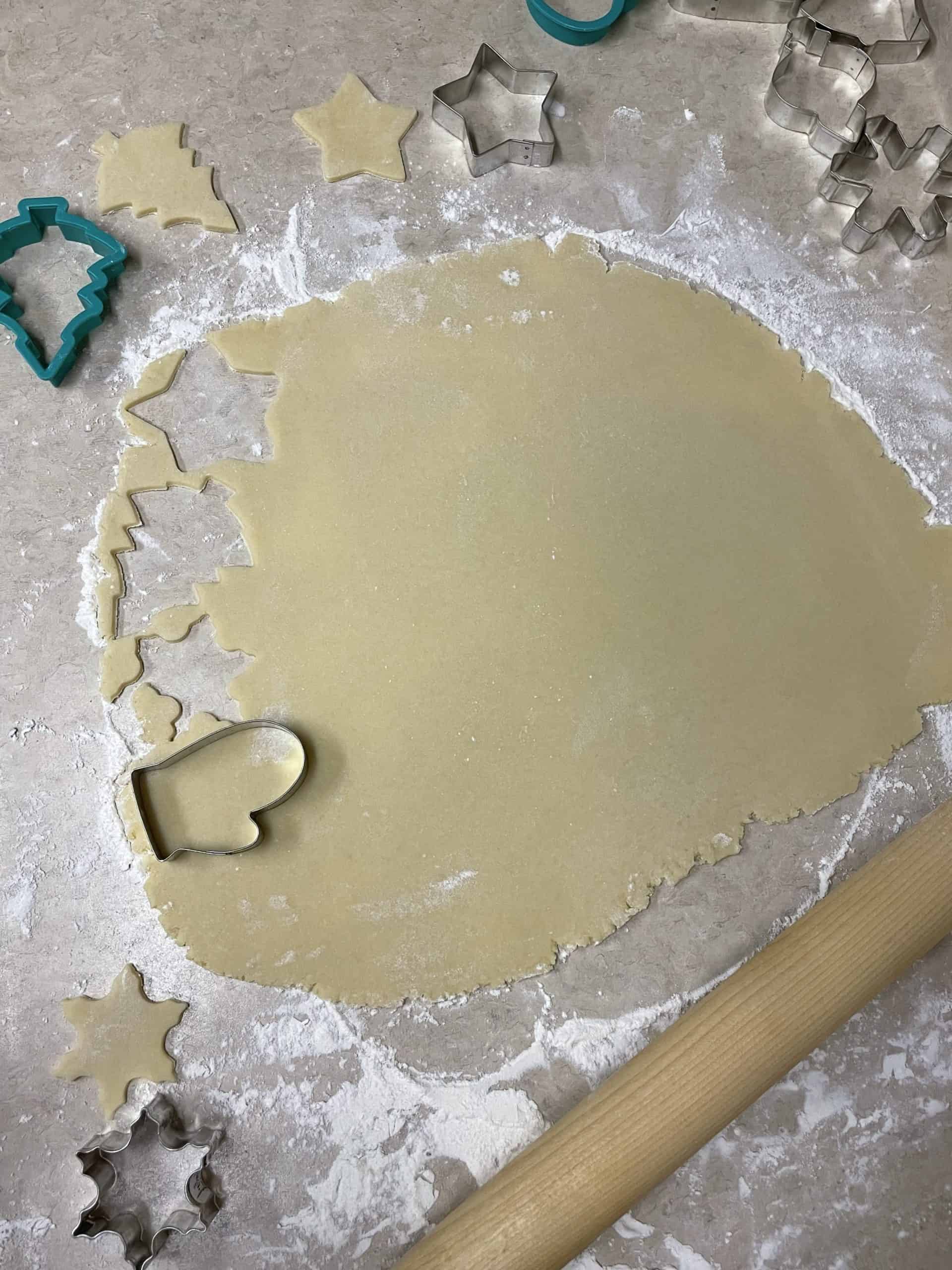 Using cookie cutters to cut the rollout sugar cookie dough.
