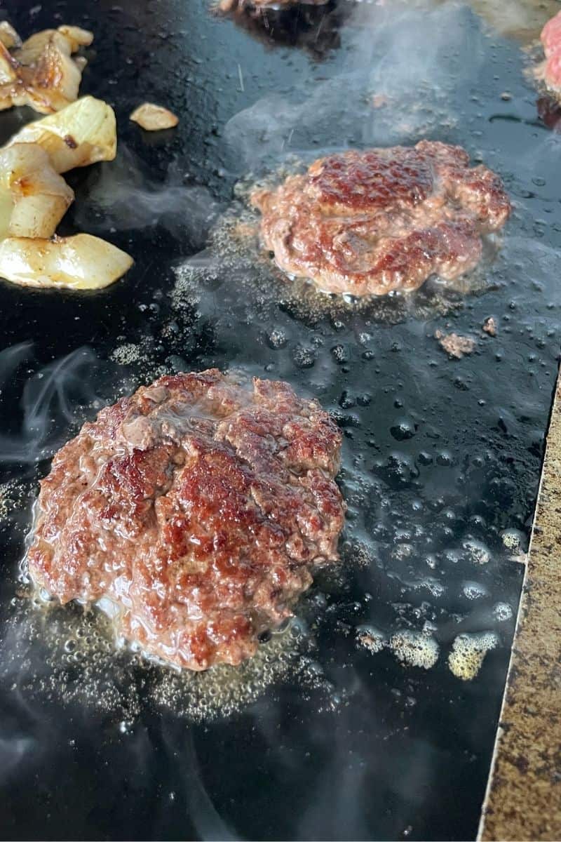 Cooking 2 Smash Burger Patties with a pile of grilled onions on a Flat Top Griddle.
