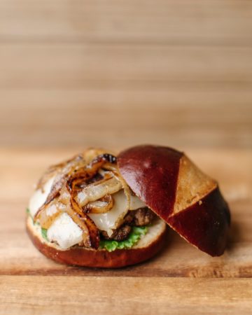 Onion Swiss Pretzel Bun Burger on a wooden cutting board.