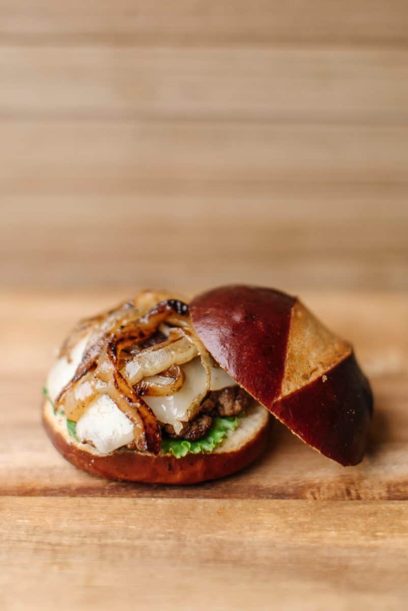 Onion Swiss Pretzel Bun Burger on a wooden cutting board.