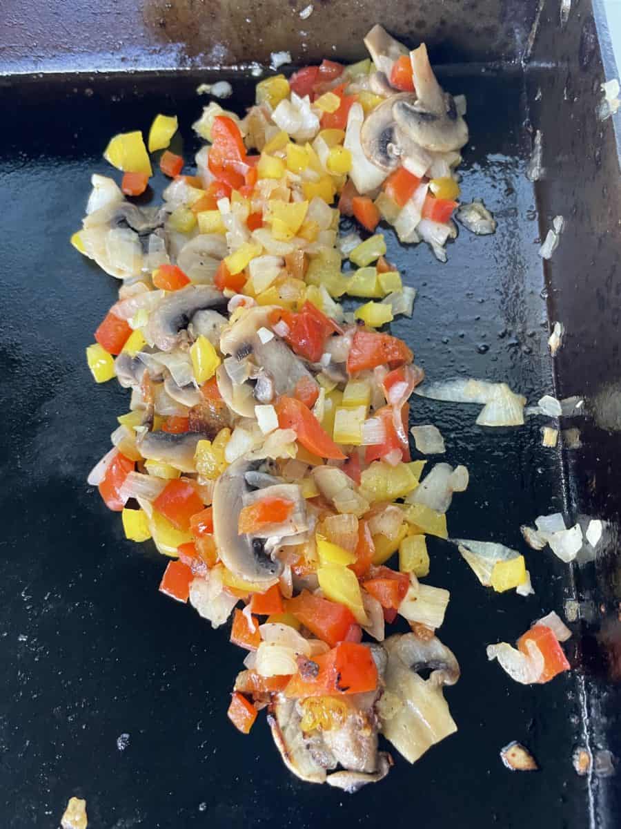 Diced peppers, onion, and sliced mushrooms cooking on a Blackstone Griddle.  