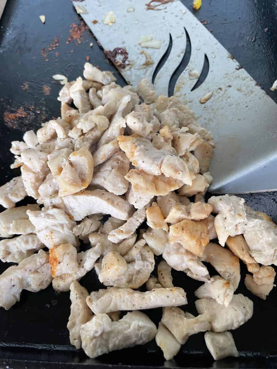 Cooked Diced Chicken Breast on a Blackstone Griddle with a griddle spatula