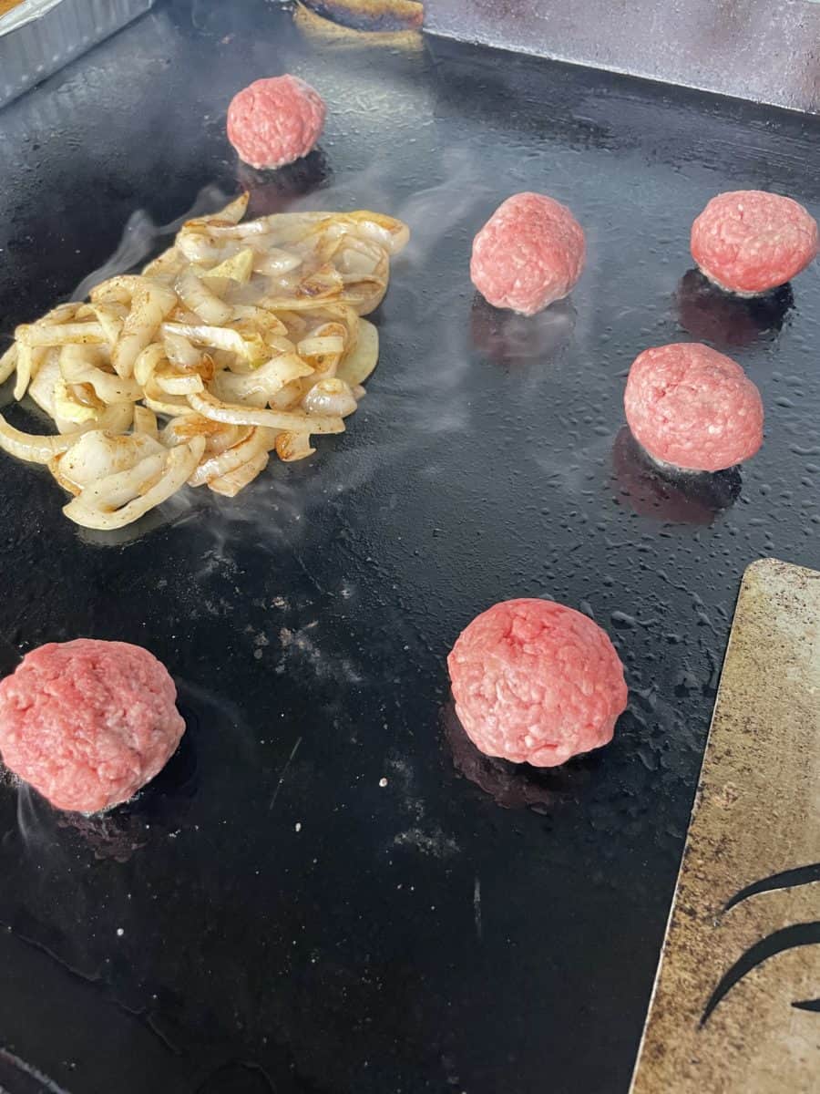 Caramelized Onions and Several Smash Burger Balls Cooking on a Blackstone Griddle.