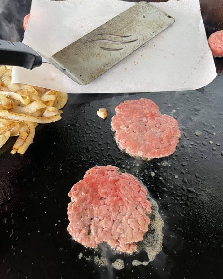 Smashing Burger on a Blackstone Griddle with cooked onions and a couple of burger patties.