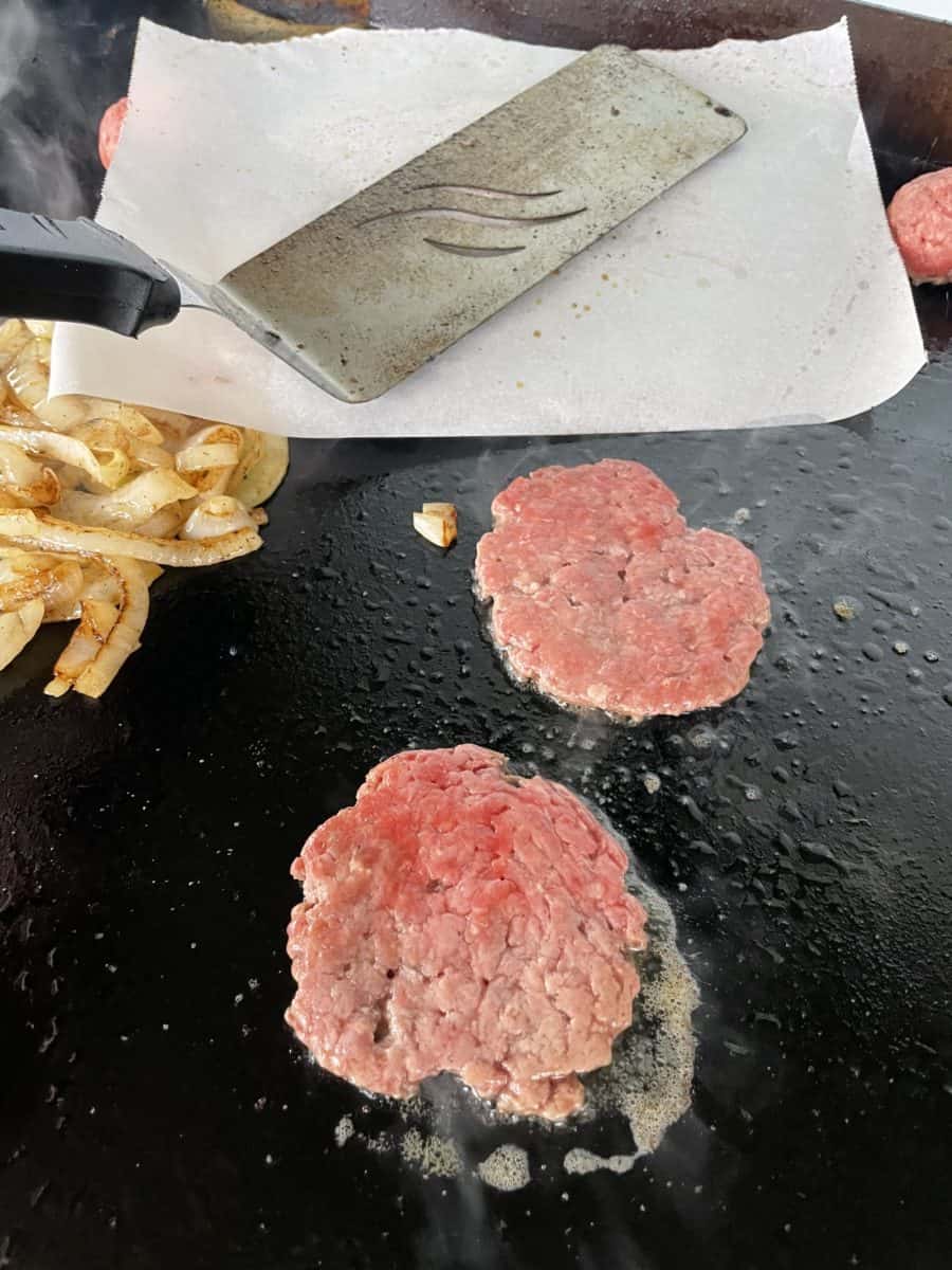Smashing Burger on a Blackstone Griddle with cooked onions and a couple of burger patties.