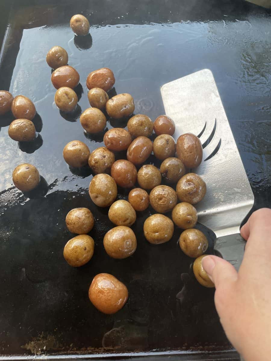 Arranging Baby Potatoes on a Blackstone Griddle with a spatula.