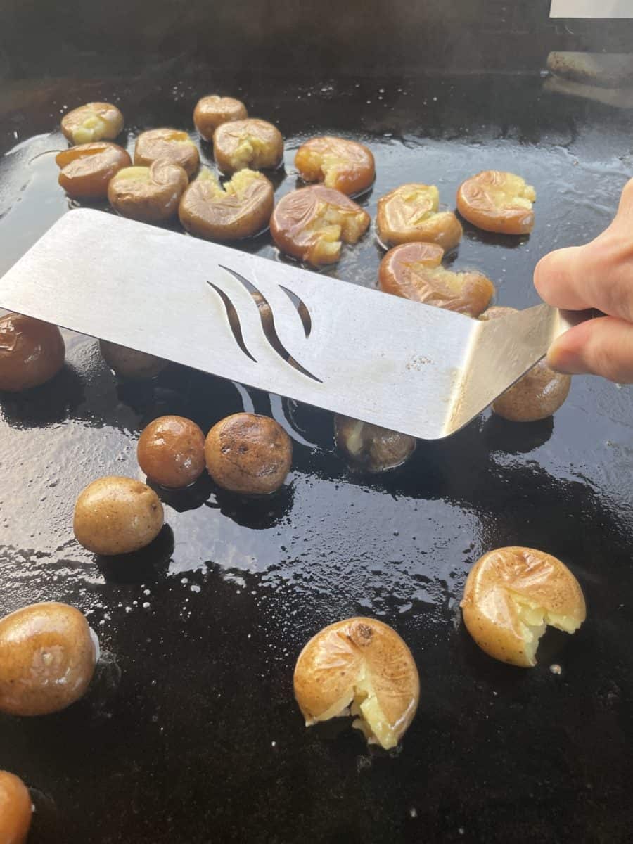 Smashing Baby Potatoes on a Blackstone Griddle with a griddle spatula.