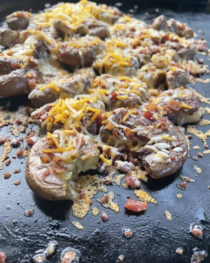 Blackstone Smashed Potatoes with Cheese and Bacon cooking on a flat top griddle.