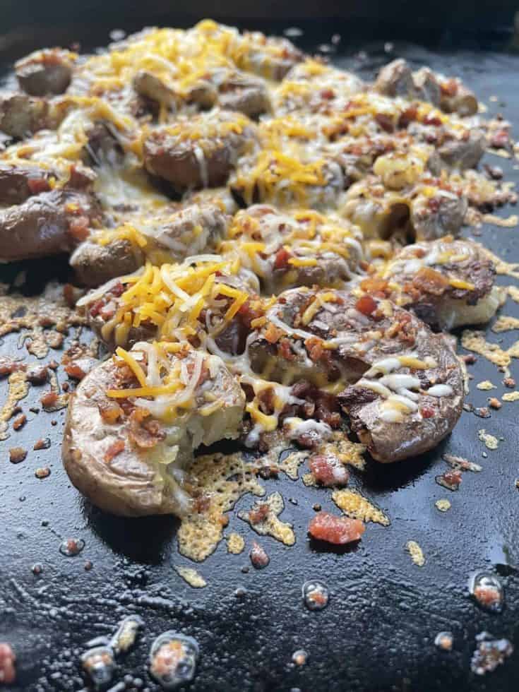 Blackstone Smashed Potatoes with Cheese and Bacon cooking on a flat top griddle.