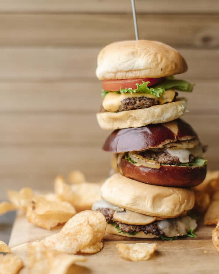 Burger Tower surrounded by kettle potato chips all on a wooden cutting board.