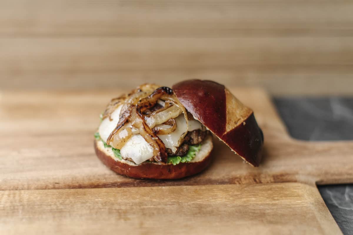 Blackstone Griddle cooked Onion Swiss Pretzel Bun Burger on a wooden cutting board.