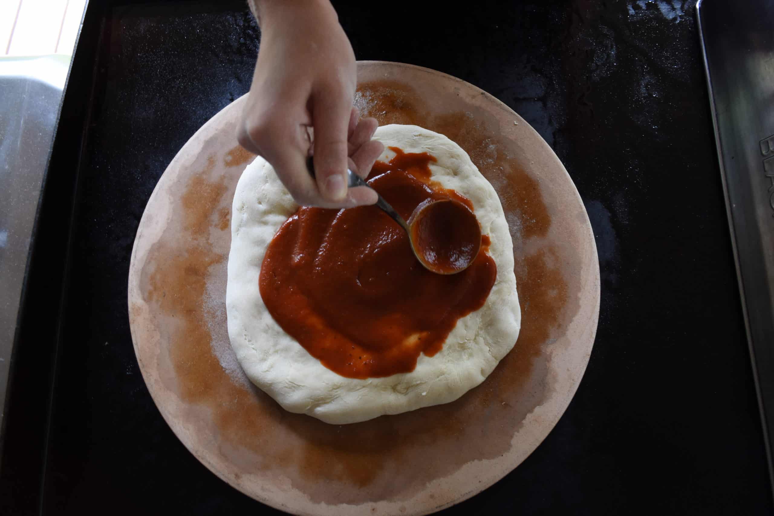 Spreading pizza sauce on to the round pizza dough.