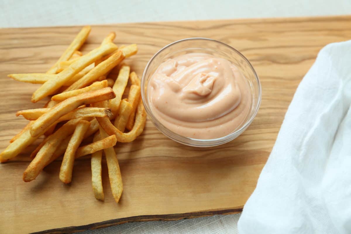 Ketchup and Mayo Sauce in a glass bowl with French Fries all on a wooden board with a white linen napkin.
