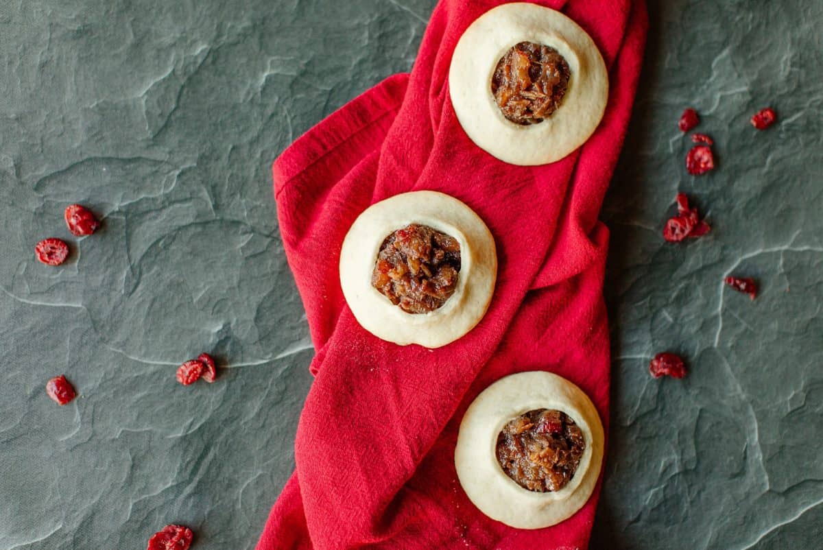 3 Cranberry Cookies on a red linen napkin with dried cranberries scattered around a black map.
