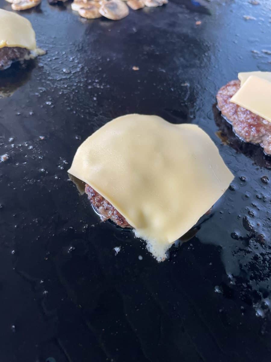 A Smashed Burger Topped with a Slice of American Cheese that is bring cooked on a Flat Top Griddle.