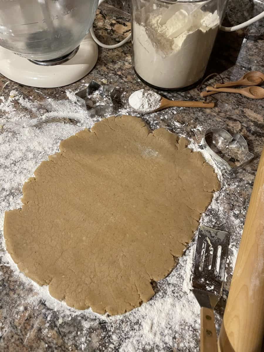 Rolled out pumpkin spice cutout cookies on a floured surface surrounded by a mixer, flour and rolling pin.