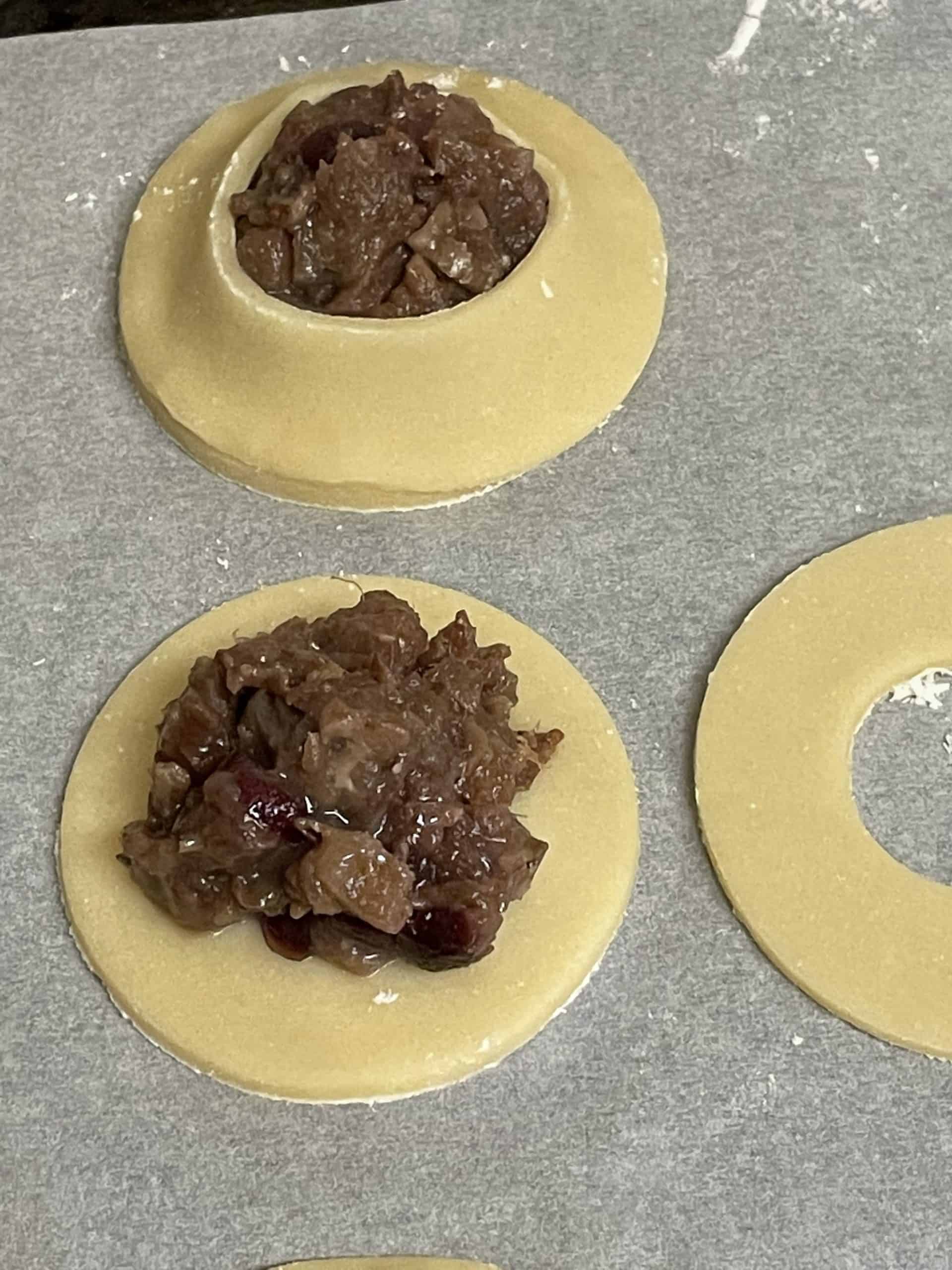 One fully assembled unbaked cranberry cookie along with the cookie parts: dough circle with filling on top along with a doughnut cut out dough piece.
