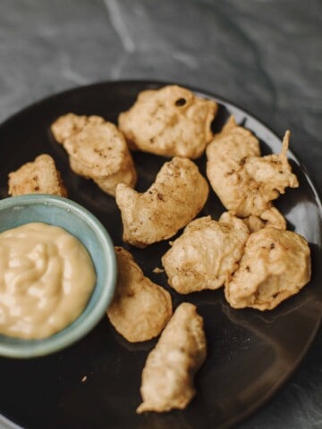 Tempura Chicken Nuggets on a black plate with a small bowl of dipping sauce.
