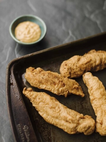 Easy Chicken Tempura Strips on a baking sheet with a side of mayo and ketchup recipe.