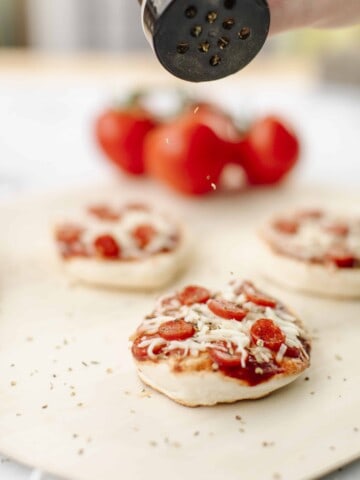 Mini Pizzas cooked on a Blackstone Griddle. Displayed on a wooden pizza peel with a cluster of tomatoes in the background.
