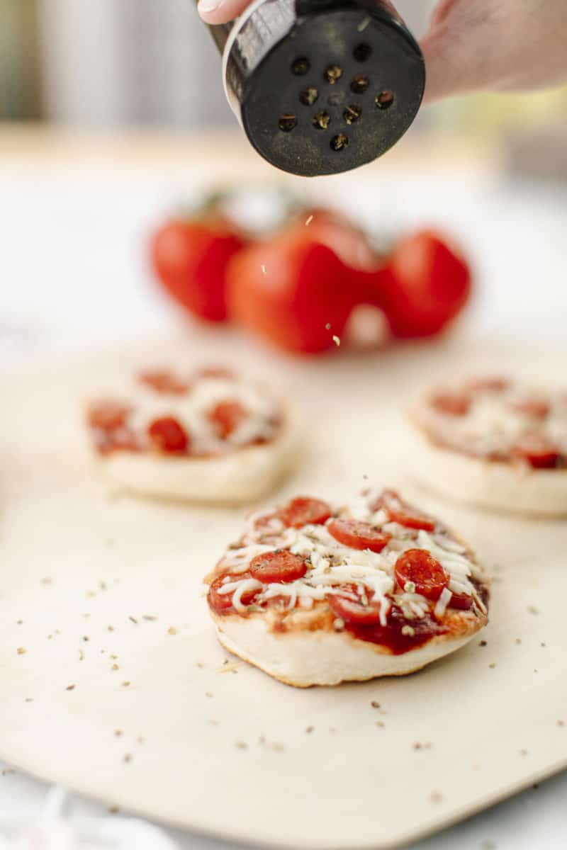 Mini Pizzas cooked on a Blackstone Griddle.  Displayed on a wooden pizza peel with a cluster of tomatoes in the background.
