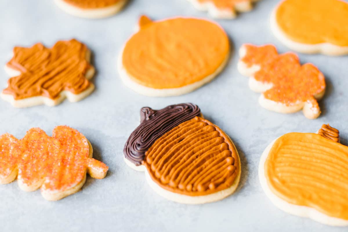 Pumpkin Spice Cookie Recipe (an assortment of fall cream cheese frosted cut out cookies on a mat). 
