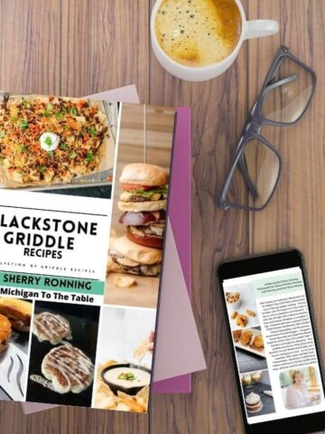 Blackstone Griddle Recipes E-Cookbook on a stack of other books along with a cellphone, eye glasses, and a cup of coffee.