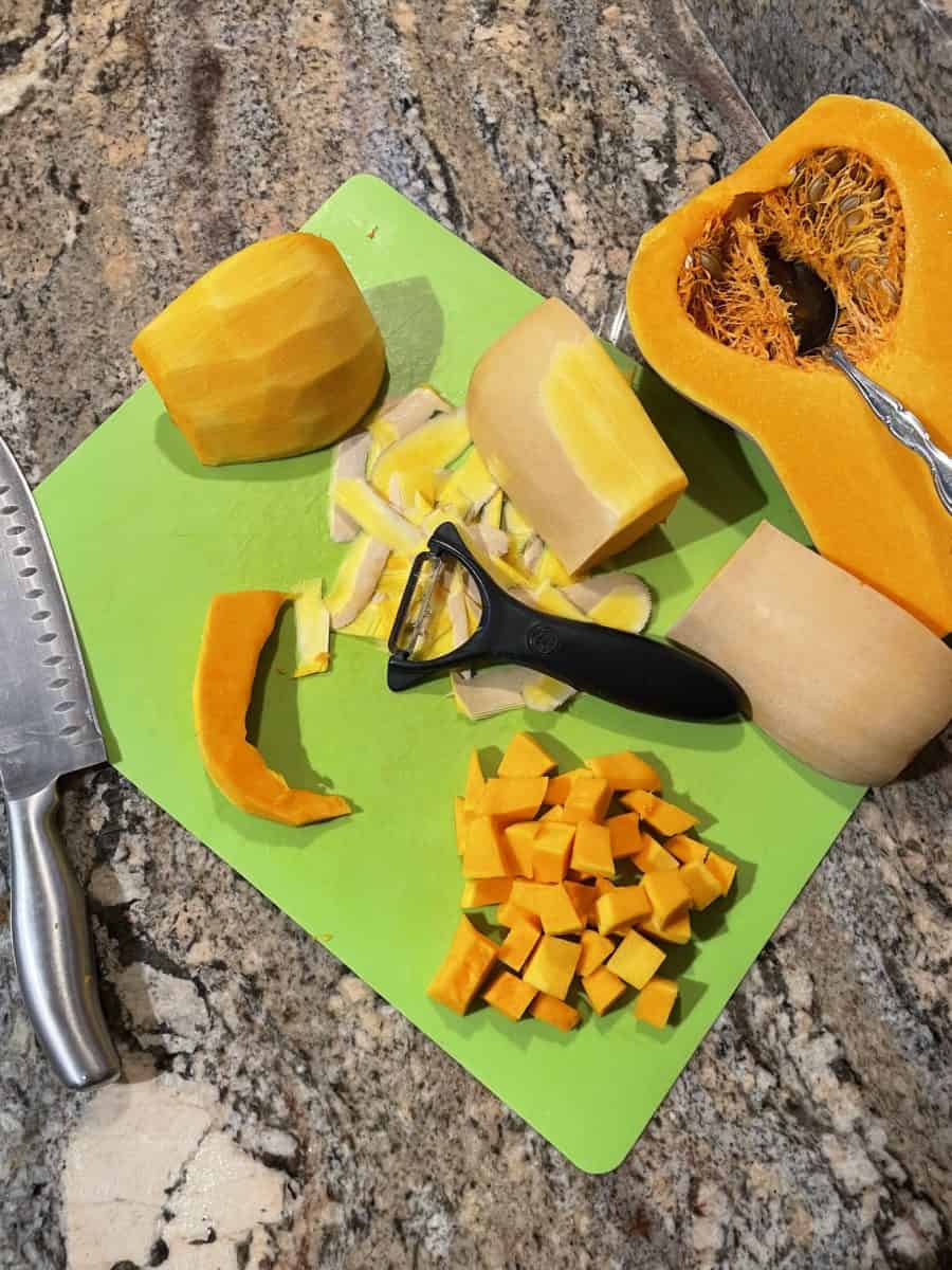 How to Peel and Dice Butternut Squash on a green cutting mat with a sharp knife, spoon, and a peeler