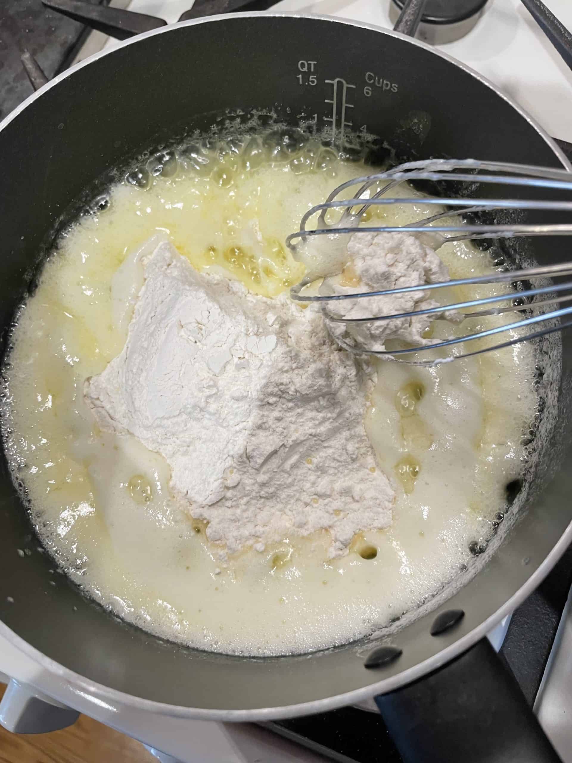 Adding flour to the melted butter in a saucepan with a whisk.