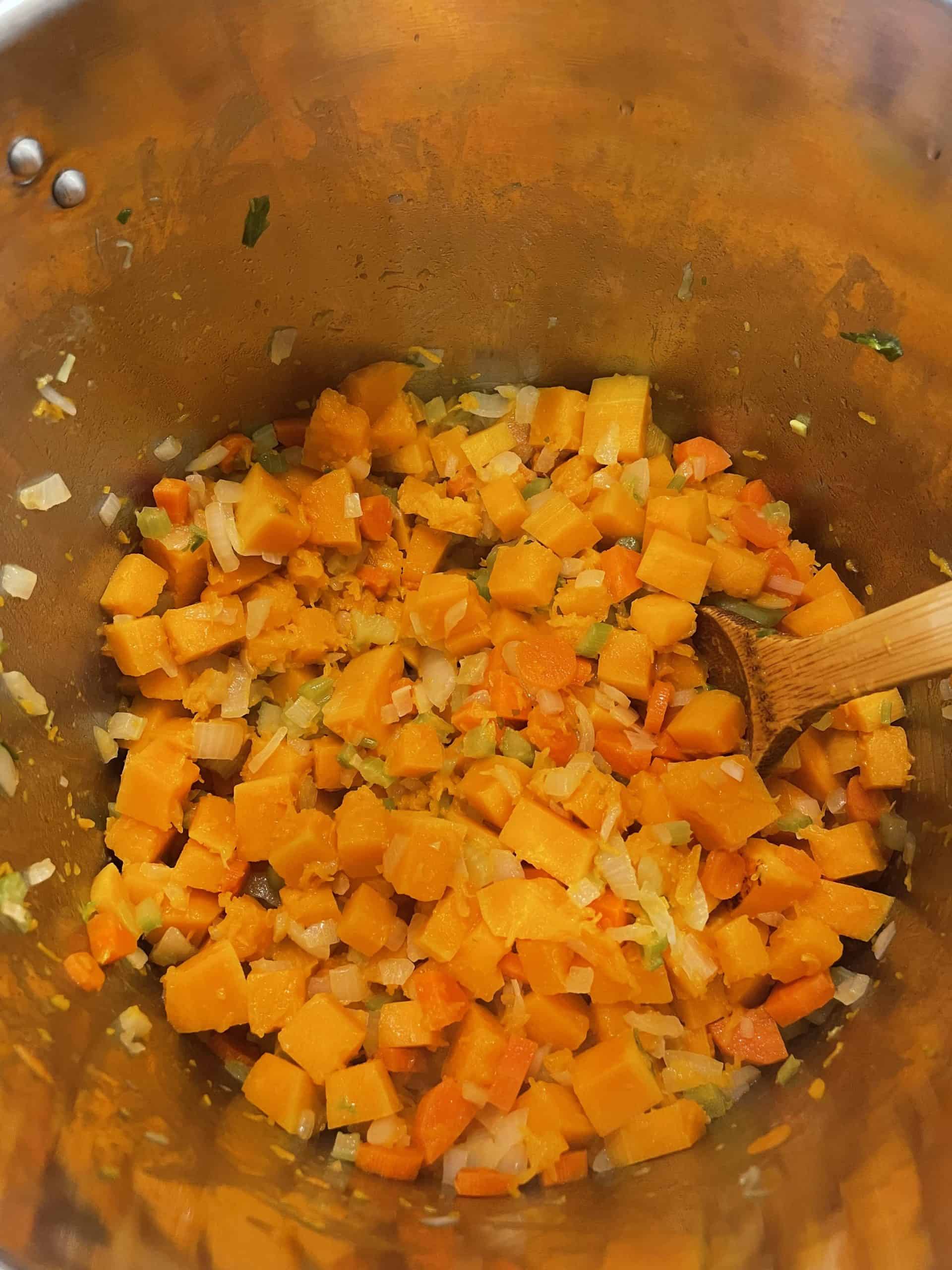 Sautéing the diced carrots, celery, onions, and butternut squash in a large stock pot. 