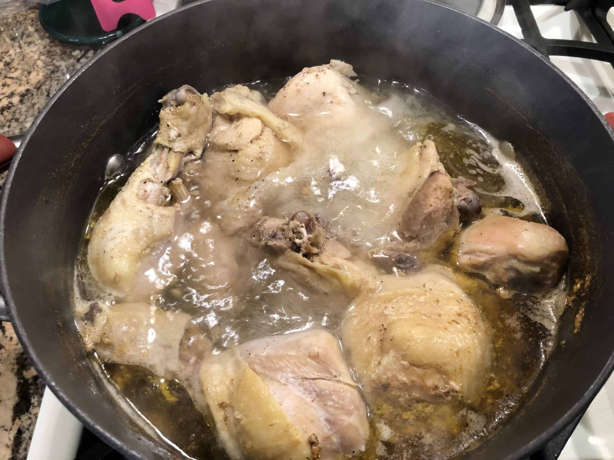 Chicken pieces boiling in seasoned water in a pot on the stove.