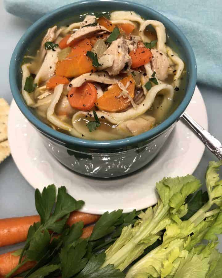Chick Fil A Chicken Noodle Soup (Copycat) in a bowl surrounded by celery, carrots, parsley, and saltine crackers.