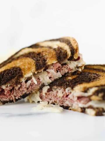 Blackstone Corned Beef Reuben Sandwich cut in half and stacked together with a side of sauerkraut.