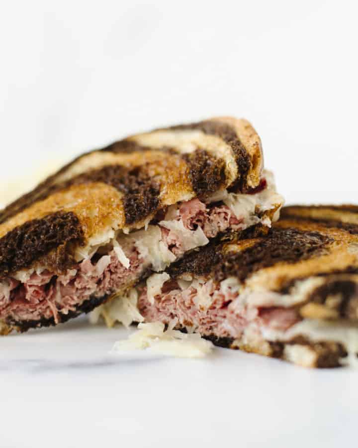 Blackstone Corned Beef Reuben Sandwich cut in half and stacked together with a side of sauerkraut.