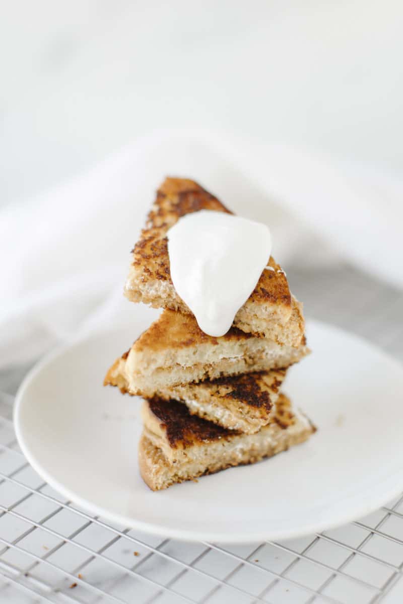Blackstone Grilled Fluffernutter Sandwich cut into triangles and stacked on a white plate and topped with some Marshmallow Creme.