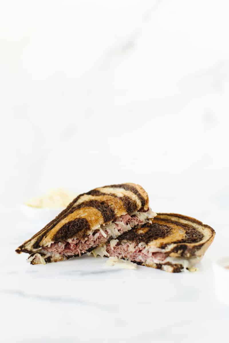 Corned Beef Reuben Sandwich cut in half and stacked together with a side of sauerkraut and Thousand Island dressing. 
