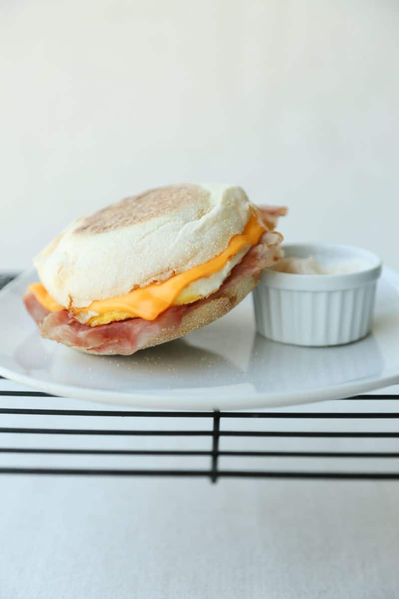 Ham Egg and Cheese Sandwich on a plate on a wire rack with a small cup of mayo.
