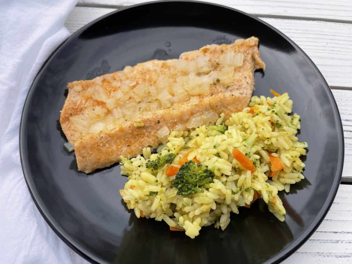 Baked Trout Filet on a plate with chicken rice and vegetables.