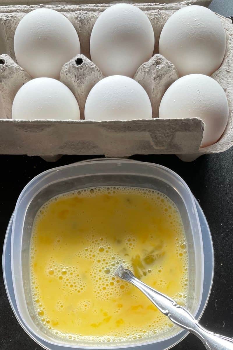 Uncooked Scrambled Eggs in a bowl along with a carton of white eggs.